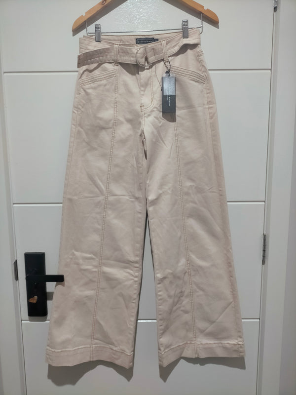 Beige pants hanging on a wooden hanger against a white tiled wall.