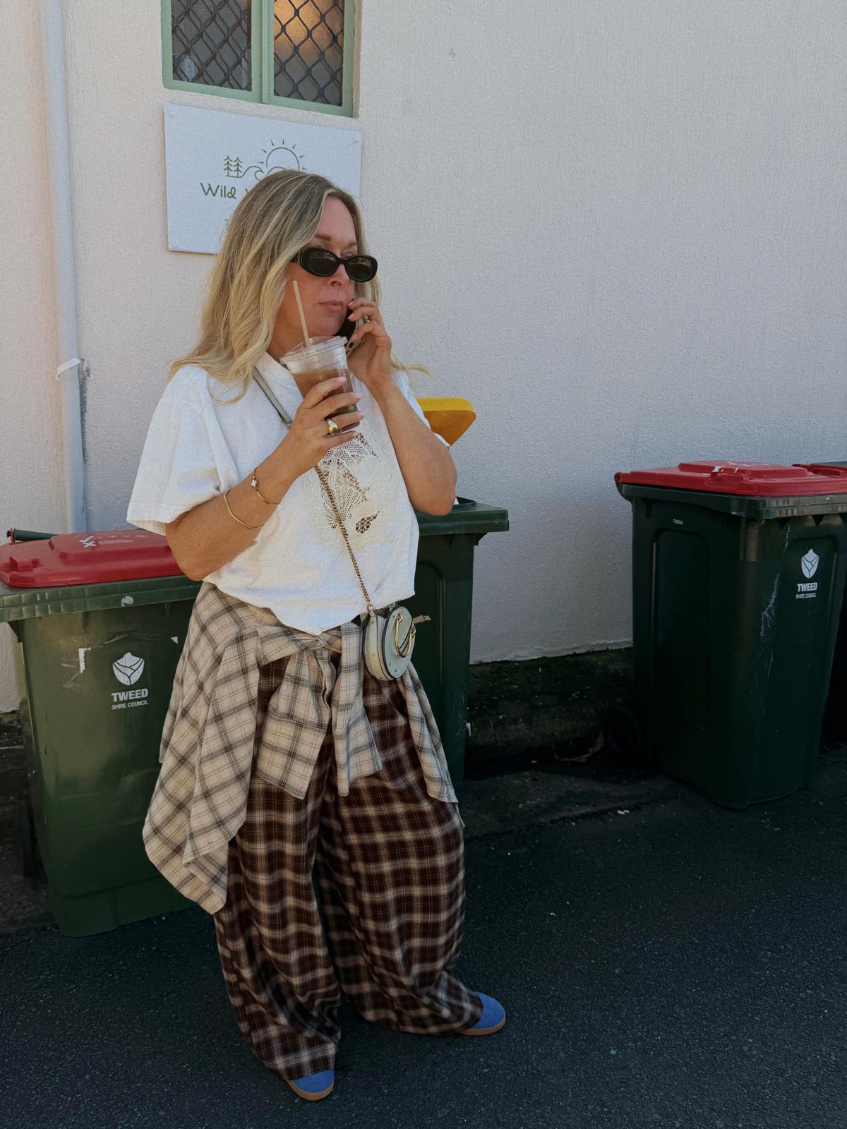 Jaase Stevie Austin Flannel Pants chocolate – outdoor lifestyle shot with model on phone holding iced coffee