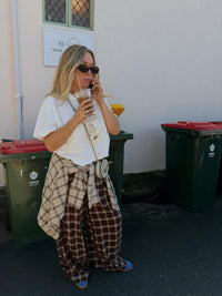 Jaase Stevie Austin Flannel Pants chocolate – outdoor lifestyle shot with model on phone holding iced coffee