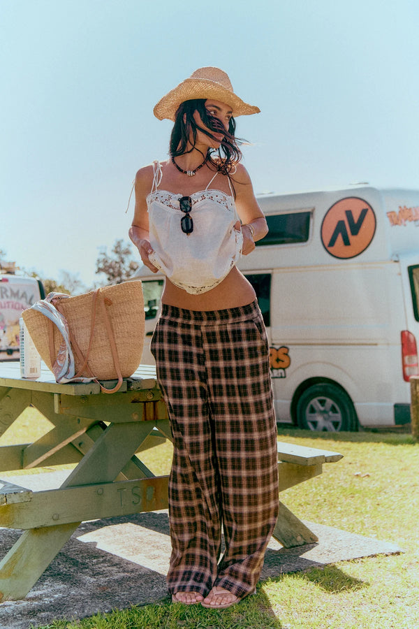 Jaase Stevie Austin Flannel Pants chocolate by Jaase – model standing outdoors at beach with cowboy hat and cami top lifted up to show details of pants