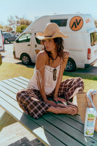 Jaase Stevie Austin Flannel Pants chocolate by Jaase – model sitting on beach park bench cowboy hat and white cami top with thongs outdoor lifestyle shot