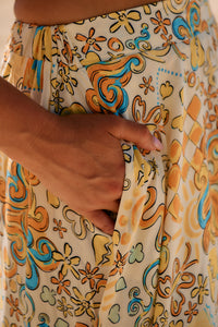 Close-up of a person wearing the Sonnie print which is a buttery yellow colorful patterned maxi skirt with a hand showing it has pockets.